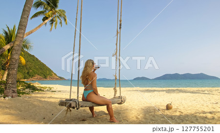 Seductive woman swinging on a swing on a tropical beach, on shores of the turquoise sea. Concept travel, walks, rest in sea, tropical resort coastline relaxation traveling tourism summer holidays. 127755201