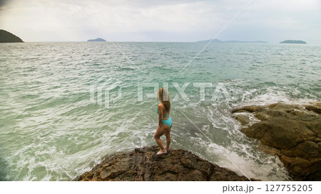 Woman chill relax resting on rock of sea reef stone, stormy cloudy ocean. Woman in swimsuit dress tunic. Concept rest tropical outdoor tourism 127755205