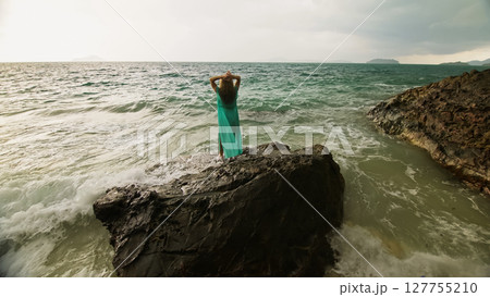 Woman walks on rock of sea reef stone, stormy cloudy ocean. Blue swimsuit dress tunic. Concept rest, tropical resort coastline tourism summer holidays 127755210