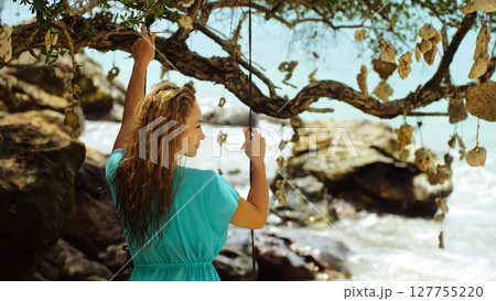 Sexy woman spends her vacation at the seaside. The girl is swinging on a swing. Concept happy holidays, joy, lightness, fresh air, cleanliness and health. Sexy woman spends her vacation at the seaside. The girl is swinging on a swing. Concept happy holidays, joy, lightness, fresh air, cleanliness and health. 127755220
