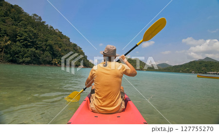 Man with sunglasses and hat rows pink plastic canoe along sea ag Man with sunglasses and hat rows pink plastic canoe along sea ag 127755270