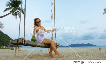 Sexual woman spends her vacation at the seaside. The girl is swinging on a swing. 127755273