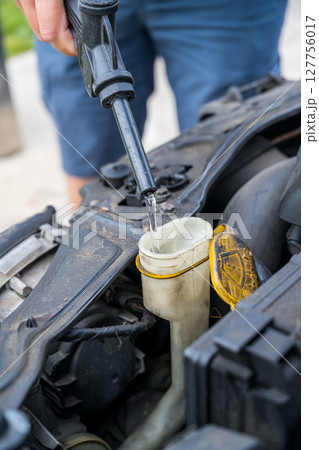 Man filling water into windscreen water tank in car engine room, for window wiper Man filling water into windscreen water tank in car engine room, for window wiper 127756017