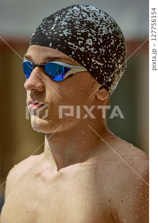 Focused swimmer wearing cap and goggles prepares for competition in outdoor pool setting 127756154