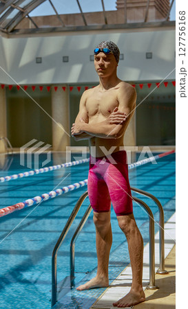 Competitive swimmer standing confidently beside indoor pool ladder 127756168