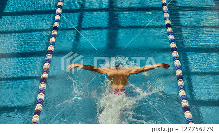 Swimmer performing butterfly stroke in competition pool lane overhead view 127756279
