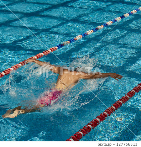 Swimmer executing butterfly stroke in outdoor swimming pool lane during sunny day practice Swimmer executing butterfly stroke in outdoor swimming pool lane during sunny day practice 127756313