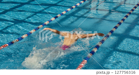 Competitive swimmer practicing butterfly stroke in clear blue swimming pool lanes Competitive swimmer practicing butterfly stroke in clear blue swimming pool lanes 127756316
