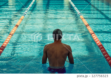 Swimmer preparing for race in indoor pool with clear lanes and blue water Swimmer preparing for race in indoor pool with clear lanes and blue water 127756323