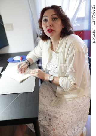 Businesswoman writing notes at desk in office environment 127756325