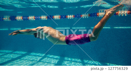 Male swimmer gliding underwater in swimming pool with sunlight casting patterns on pool floor Male swimmer gliding underwater in swimming pool with sunlight casting patterns on pool floor 127756329
