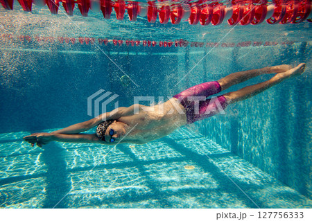 Young swimmer in goggles gliding underwater in pool with vibrant colors and sunlit ripples 127756333