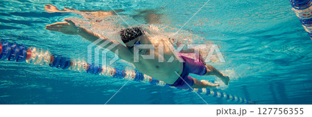 Male swimmer performing freestyle stroke in clear blue swimming pool Male swimmer performing freestyle stroke in clear blue swimming pool 127756355