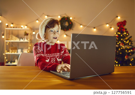 Surprised boy using laptop, choosing presents online, playing games or reading email from Santa 127756591