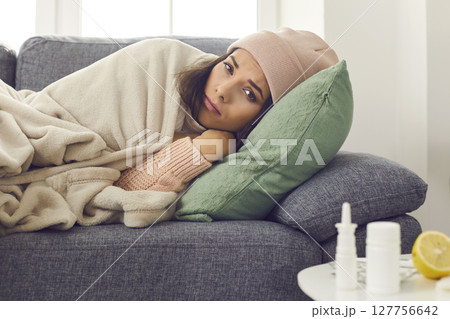Young unhappy woman in warm clothes and hat lying in bed under blanket and feeling ill 127756642