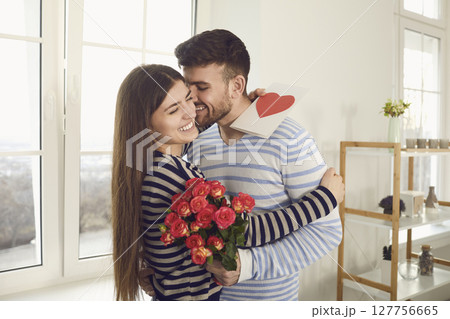 Valentine's day. The guy gives a Valentine with a red heart to a girl standing at the window in the room 127756665
