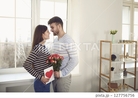 Valentine's day. The guy gives a Valentine with a red heart to a girl sitting on a sofa in the room Valentine's day. The guy gives a Valentine with a red heart to a girl sitting on a sofa in the room 127756756