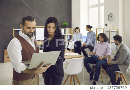 Man in an office shows a report to a young woman to his boss. 127756769