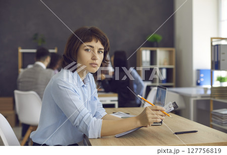 Portrait of businesswoman sitting at office desk, holding clipboard and looking at camera 127756819