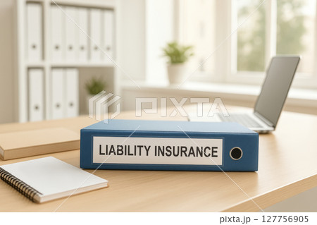 Liability insurance concept shown by blue binder on wooden desk in bright office with laptop and notebook, representing business protection and risk management 127756905