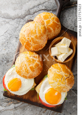 Chinese pineapple bun sandwich with fried egg, butter, tomato, cheese, lettuce close-up on wooden board. Vertical top view Chinese pineapple bun sandwich with fried egg, butter, tomato, cheese, lettuce close-up on wooden board. Vertical top view 127757023