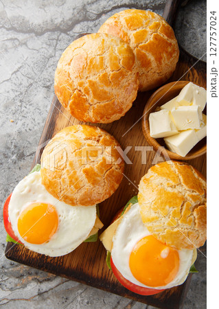 Bolo bao bun sandwich with fried egg, butter, tomato, cheese, lettuce close-up on wooden board. Vertical top view Bolo bao bun sandwich with fried egg, butter, tomato, cheese, lettuce close-up on wooden board. Vertical top view 127757024