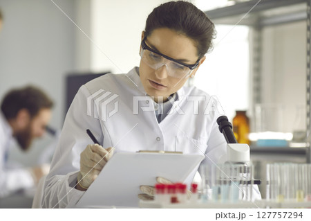 Scientist taking notes while doing medical research in modern science laboratory 127757294