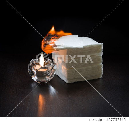 A burning candle lit the napkins on the table A burning candle lit the napkins on the table 127757343