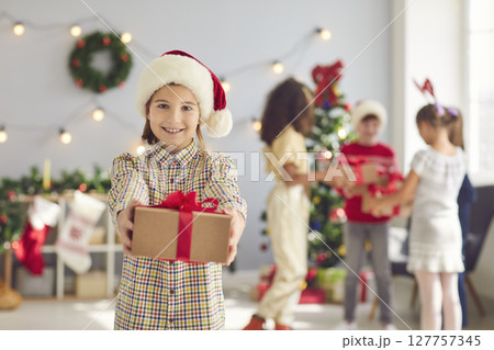 Happy girl holding out hands with Christmas present, looking at camera and smiling Happy girl holding out hands with Christmas present, looking at camera and smiling 127757345