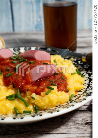 Creamy polenta with tomato sauce, sausage and chives on rustic wooden table 127757420