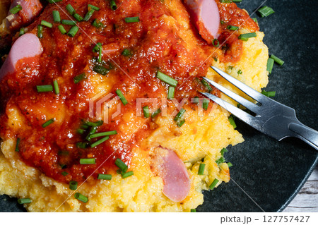 Creamy polenta topped with sausage ragu, fresh chives, and a fork ready to eat 127757427