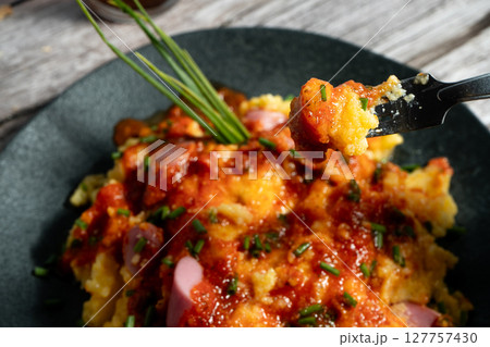 Fork lifting delicious bite of creamy polenta with sausage and tomato sauce 127757430