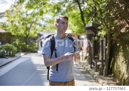 緑に包まれた参道でスマートフォンを持って立ち止まる男性 127757861