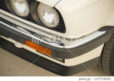 A detailed closeup of a classic vintage BMW e30 white cars front end showcasing chrome detailing and bright headlights A detailed closeup of a classic vintage BMW e30 white cars front end showcasing chrome detailing and bright headlights 127758092