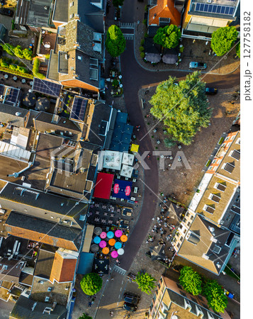 Top-down aerial view of a lively European street scene with colorful umbrellas, outdoor cafes, and traditional buildings surrounding a tree-lined cobblestone plaza. Top-down aerial view of a lively European street scene with colorful umbrellas, outdoor cafes, and traditional buildings surrounding a tree-lined cobblestone plaza. 127758182