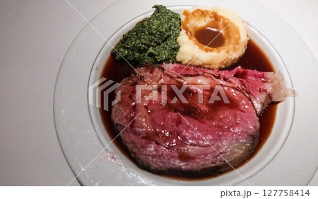 Title: close up of a medium rare prime rib beef steak with mashed potato and spinach on the side barbecue gravy sauce on a white plate with copy space Title: close up of a medium rare prime rib beef steak with mashed potato and spinach on the side barbecue gravy sauce on a white plate with copy space 127758414