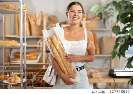 Positive young girl holding baguettes in plastic bag in bakery Positive young girl holding baguettes in plastic bag in bakery 127758639
