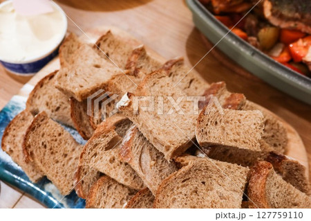 close up of a neatly arranged stack of sliced brown bread, likely whole grain or rye, displayed on a wooden board, with butter on the side 127759110