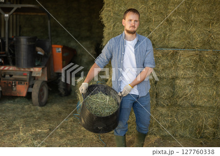 Young man with bucket of hay in barn Young man with bucket of hay in barn 127760338