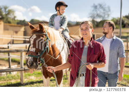 Young woman leading horse with boy on horseback 127760378