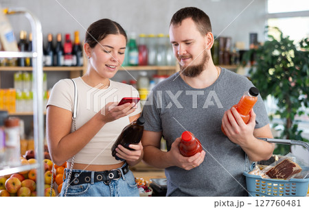 Portrait of man and woman checking the expiration date of juice using smartphone 127760481