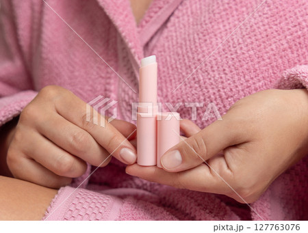 Woman in pink bathrobe holding in hand opened lip balm stick with a lid closeup, girly mockup Woman in pink bathrobe holding in hand opened lip balm stick with a lid closeup, girly mockup 127763076
