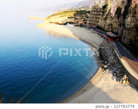 Stunning aerial view of the coastline in Tropea, Italy, showcasing the crystal-clear turquoise sea gently lapping against the golden sandy beach. The cliffs rise majestically above the shoreline 127763774