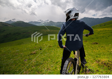 Male athlete cyclist in helmet and protective mask outdoors. MTB rider in mountainous terrain against the backdrop of epic rocks. 127763804