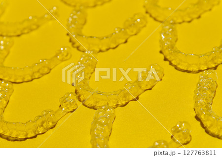 Clear dental aligners on colored yellow background, close-up side view from above. Pattern of clear braces Clear dental aligners on colored yellow background, close-up side view from above. Pattern of clear braces 127763811