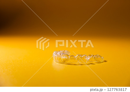 Transparent dental aligners on a colored yellow background, close-up, side view. Modern methods to straighten teeth Transparent dental aligners on a colored yellow background, close-up, side view. Modern methods to straighten teeth 127763817