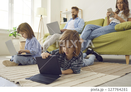 Boy lying on the floor with a tablet while the rest of the family are using their own devices Boy lying on the floor with a tablet while the rest of the family are using their own devices 127764281
