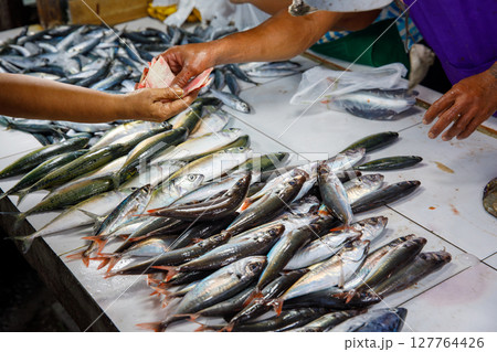 Buying fresh fish at wet market in Philippines with vendor receiving money over display of seafood on white tiles 127764426