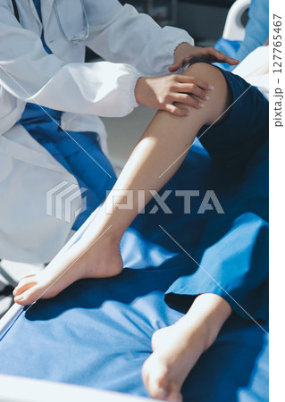 Female doctor hands doing physical therapy By extending the leg and knee of a male patient Female doctor hands doing physical therapy By extending the leg and knee of a male patient 127765467