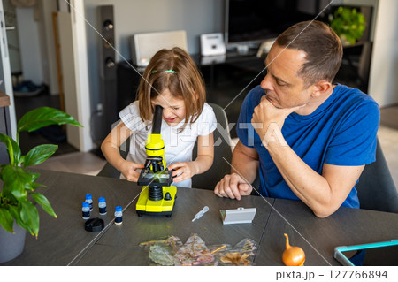 Father and daughter examining various plant samples under a microscope at home. Concept of family science education and botanical exploration Father and daughter examining various plant samples under a microscope at home. Concept of family science education and botanical exploration 127766894